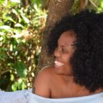 Three young African women, sat together, laughing outside.