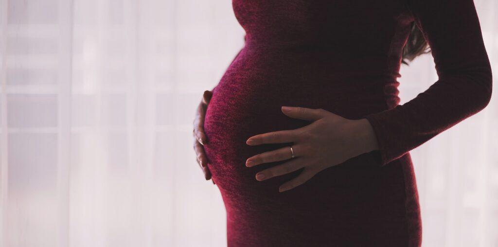 A pregnant woman in a red dress puts both hands on her belly.