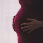 A pregnant woman in a red dress puts both hands on her belly.